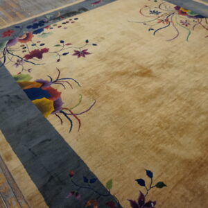 Gold high-pile rug featuring multicolored florals and a wide blue-gray border on wooden plank flooring.