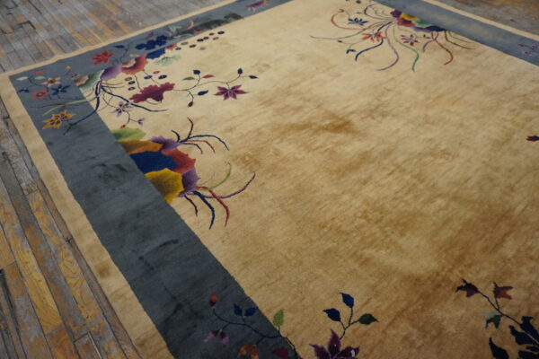 Gold high-pile rug featuring multicolored florals and a wide blue-gray border on wooden plank flooring.