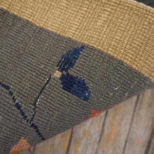 Close-up of a ribbed flatweave rug in gray, tan, and accent colors resting on aged wood.