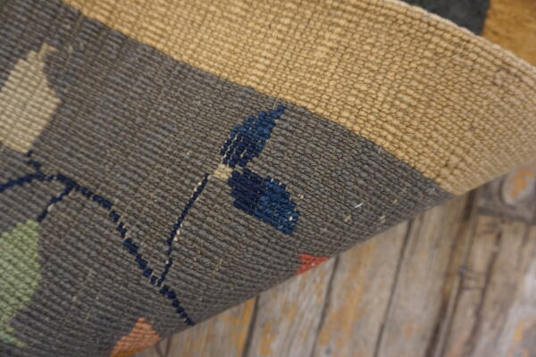 Close-up of a ribbed flatweave rug in gray, tan, and accent colors resting on aged wood.