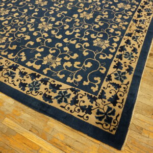 Deep blue rug with a dense tan scrolling floral pattern displayed on distressed hardwood floors.