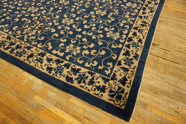Deep blue rug with a dense tan scrolling floral pattern displayed on distressed hardwood floors.