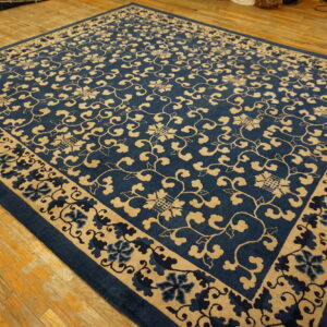 Navy and tan rug featuring an all-over scrolling vine pattern and floral border on distressed wood floors.