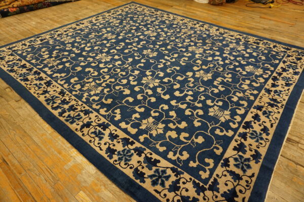 Navy and tan rug featuring an all-over scrolling vine pattern and floral border on distressed wood floors.