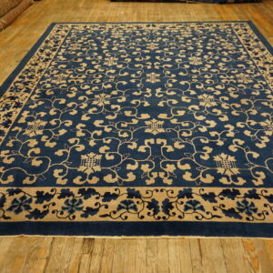 Deep indigo blue rug with beige scrolling vine patterns lies on aged wooden floorboards.