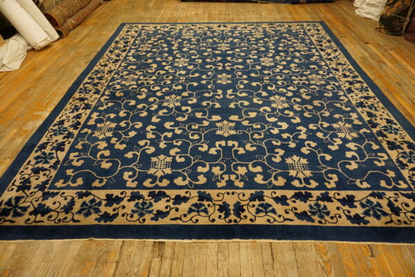 Deep indigo blue rug with beige scrolling vine patterns lies on aged wooden floorboards.