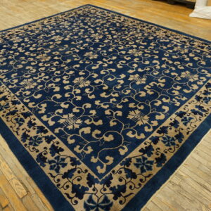 Deep blue rug with tan scrolling floral pattern lies on wide, worn wood floorboards.
