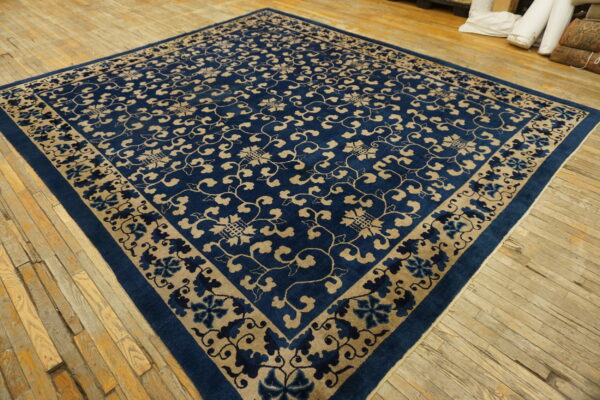 Deep blue rug with tan scrolling floral pattern lies on wide, worn wood floorboards.