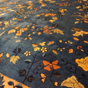 Plush blue rug featuring ornate gold and orange floral patterns and a wide contrasting orange border.