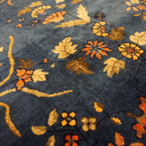 Close-up of a navy rug showing a thick floral pattern with gold, orange, and brown leaf elements.