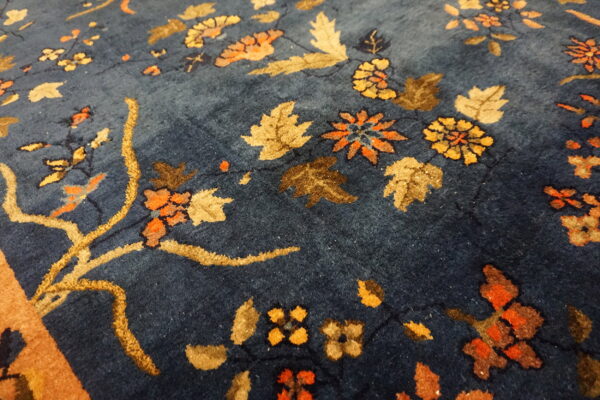 Close-up of a navy rug showing a thick floral pattern with gold, orange, and brown leaf elements.