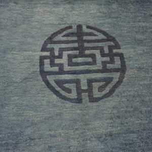 Low-pile dusty blue rug with a dark geometric circular pattern and dark blue borders.