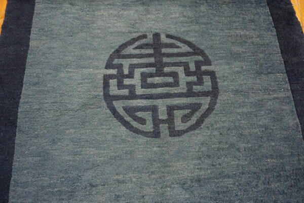 Low-pile dusty blue rug with a dark geometric circular pattern and dark blue borders.