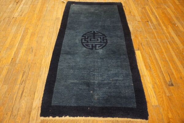 Dark blue runner rug with a thick navy border and central symbol laid on a honey-toned wood floor.