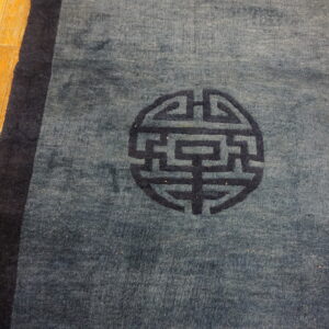 A medium blue rug with a dark blue border and central circular symbol rests on wood planks.