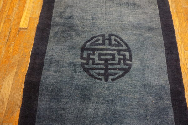 A medium blue rug with a dark blue border and central circular symbol rests on wood planks.