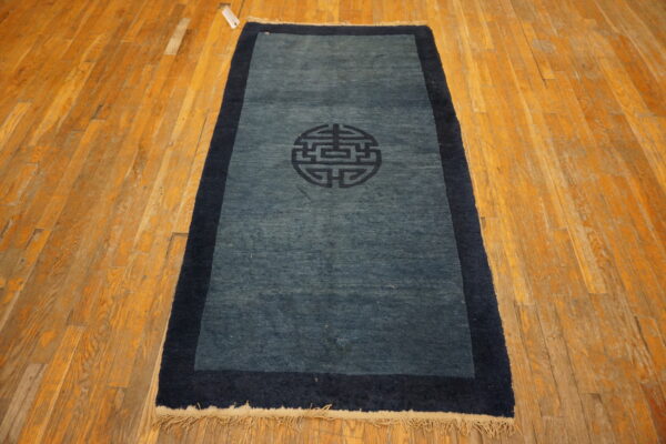A blue rug runner with a dark navy medallion and border on a distressed wood floor.
