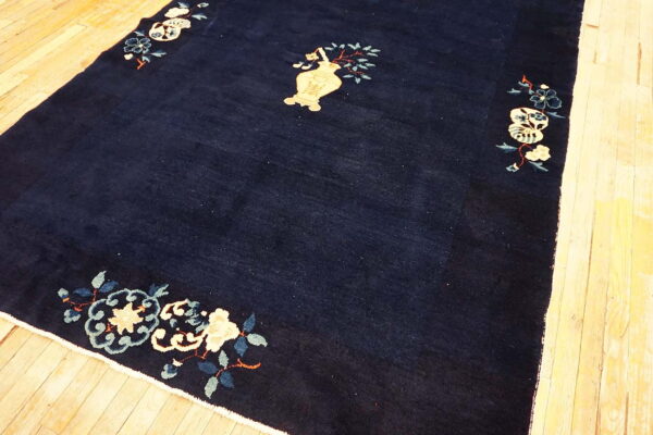 Navy rug with pale yellow vase and scattered blue floral corner designs over light wooden planks.