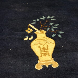 Close-up of dark blue pile rug featuring a tan vase design with stylized symbols and green leaves.
