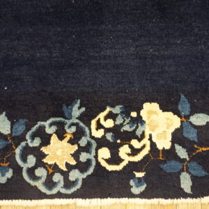 Dark blue medium-pile rug with cream and blue floral designs and white fringe resting on wood flooring.