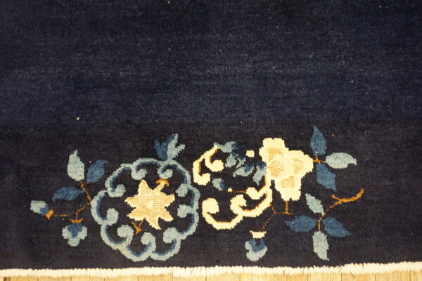 Dark blue medium-pile rug with cream and blue floral designs and white fringe resting on wood flooring.