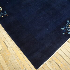 Navy blue rug with light floral corner patterns in cream and blue rests on distressed wood flooring.