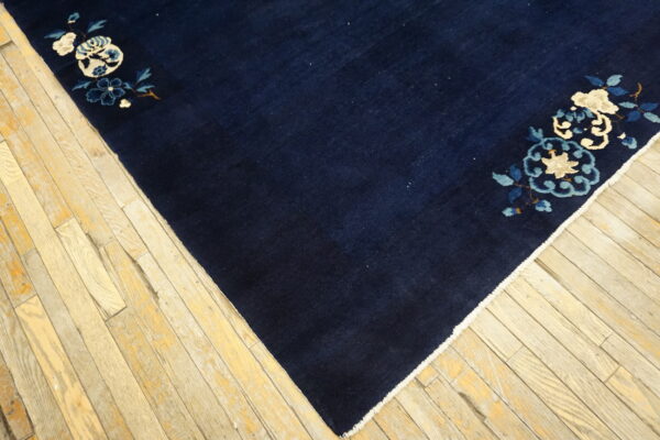 Navy blue rug with light floral corner patterns in cream and blue rests on distressed wood flooring.