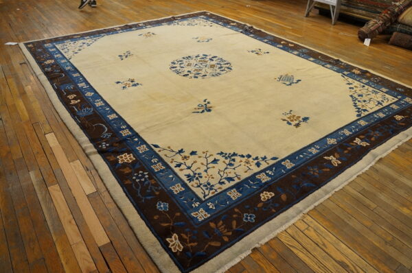 Cream area rug featuring a central medallion and broad borders in royal blue and dark brown on wood flooring.