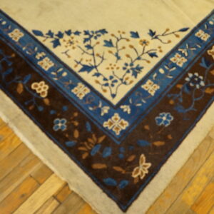 Beige rug corner with detailed floral borders in dark brown and shades of blue on light wood planks.