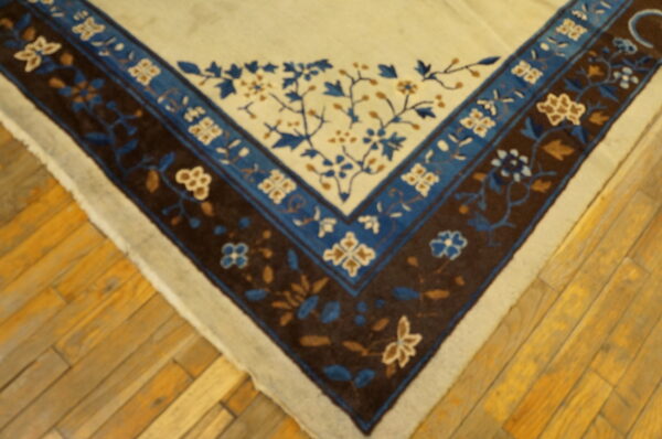 Beige rug corner with detailed floral borders in dark brown and shades of blue on light wood planks.