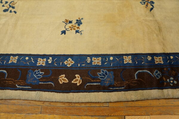 Cream rug with blue and tan florals, defined by a multi-layered brown and cobalt border over wood planks.