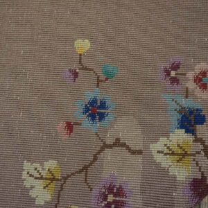 Tight flatweave taupe rug with bright, pixelated floral motifs visible over distressed wood plank flooring.