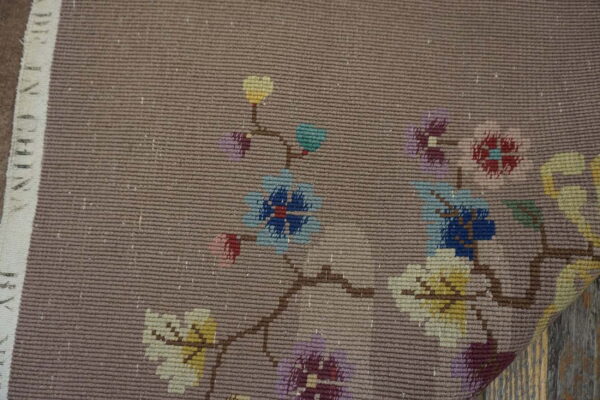 Tight flatweave taupe rug with bright, pixelated floral motifs visible over distressed wood plank flooring.