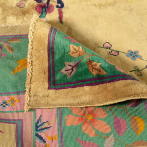 Close-up of a folded rug showing a beige floral high pile and a pink and green flat woven border.