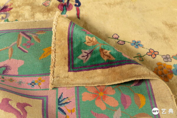 Close-up of a folded rug showing a beige floral high pile and a pink and green flat woven border.