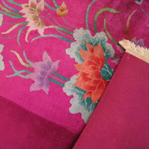 Magenta floral rug detail showing low pile, multi-colored blooms, ribbed backing, and cream fringe.
