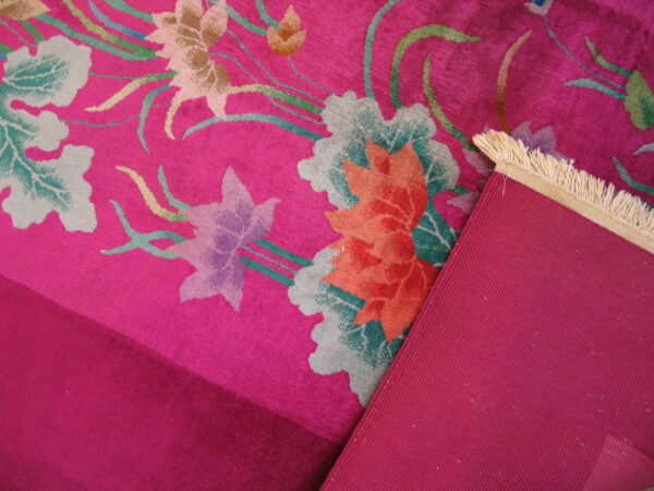 Magenta floral rug detail showing low pile, multi-colored blooms, ribbed backing, and cream fringe.