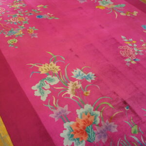 Saturated pink rug displaying multicolor botanical patterns and a darker solid border on wood floors.