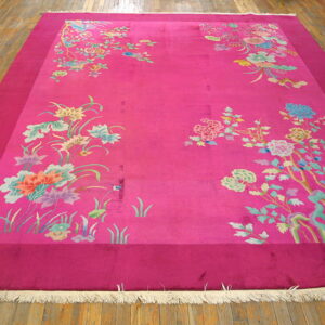 Bright pink rug featuring an inner field of scattered pastel floral motifs over wood flooring.