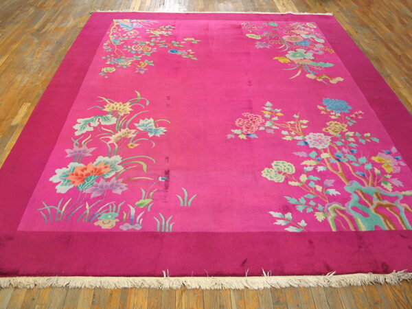 Bright pink rug featuring an inner field of scattered pastel floral motifs over wood flooring.