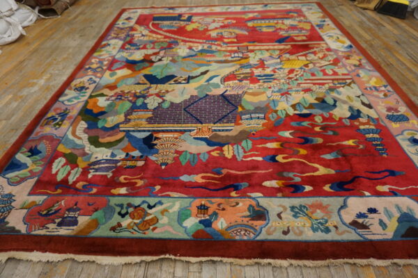 High-pile crimson rug displaying a multicolored, detailed landscape and architectural scene on a hardwood floor.