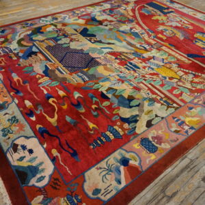 Vibrant red rug with multi-colored landscapes and patterned borders displayed on rustic wood plank flooring.