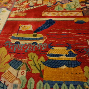 High-pile rug with a red field patterned with colorful ships, yellow buildings, and green foliage next to wood flooring.