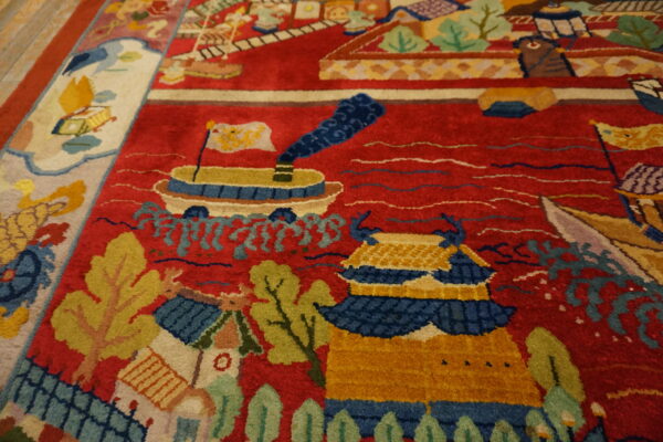 High-pile rug with a red field patterned with colorful ships, yellow buildings, and green foliage next to wood flooring.