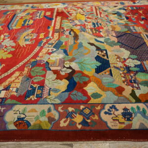 Colorful, plush rug on light wood flooring, featuring a red field with complex landscape and architectural motifs.
