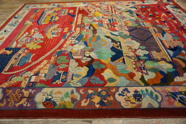 Colorful, plush rug on light wood flooring, featuring a red field with complex landscape and architectural motifs.