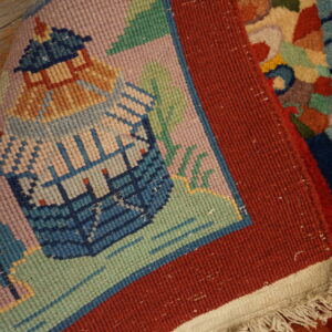 Detail of a low-pile rug showing a pink and blue pictorial field, wide red border, and white fringe.