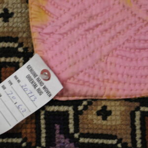 Close-up of a geometric rug pattern, pink backing fabric, and an attached white retail tag.