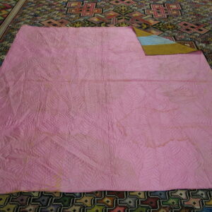 Intricate geometric multicolor rug partially covered by a large pink quilted textile.