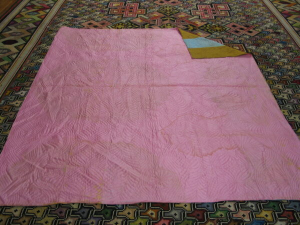 Intricate geometric multicolor rug partially covered by a large pink quilted textile.